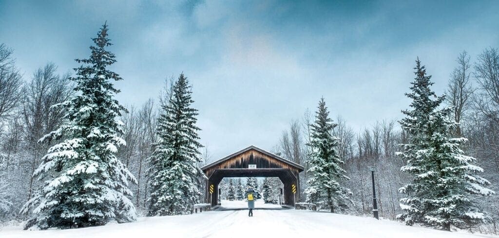 A person standing in the snow under a covered bridge. Lewiston's wooden covered bridge is literaly off the beaten track
