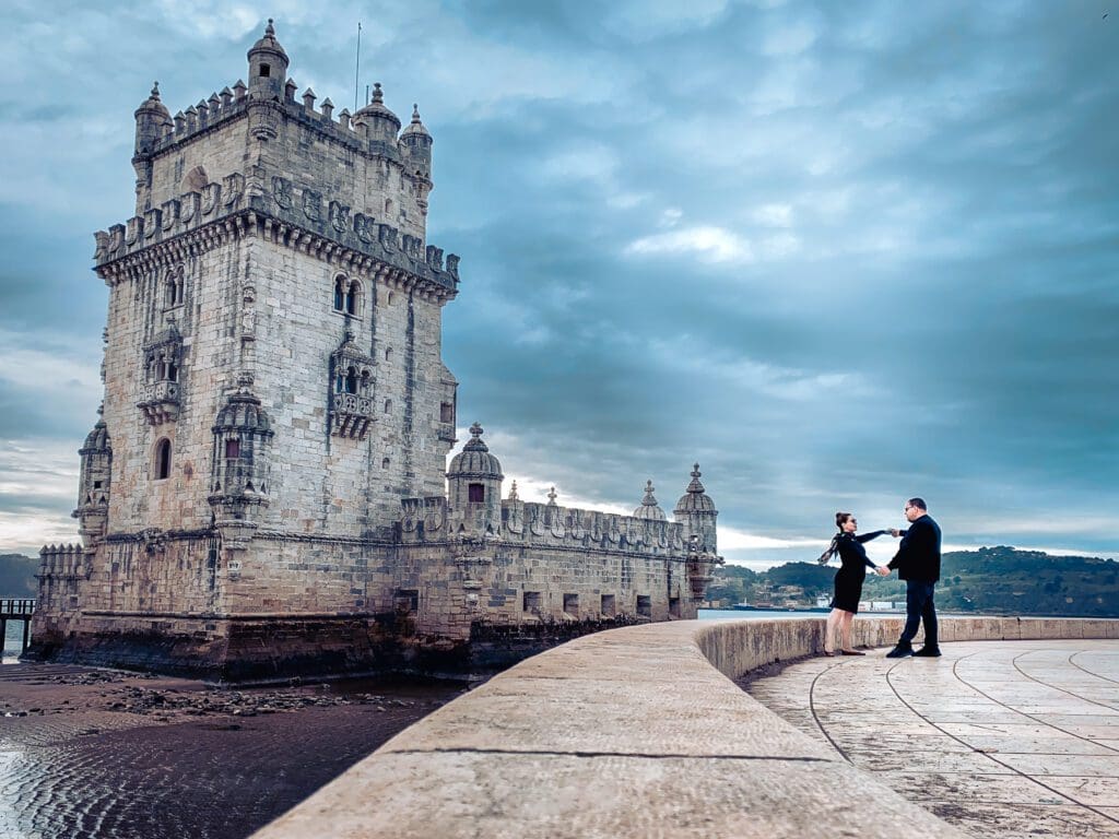 Couple posing in front of the Tower of Belem in Lisbon Portugal on a cloudy dramatic sky