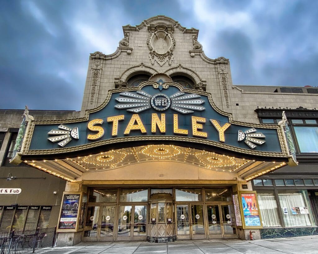 External view of the Stanley Theatre, a historic Baroque movie palace in Utica, NY, neon marquee lit up with stormy skies