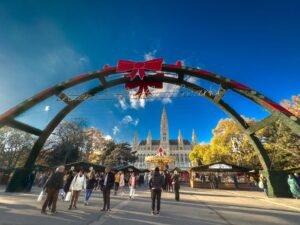 Exterior photo of a sunny winter's day infront of the decorated gates to the Rathausplatz Christkindlmarkt (Christmas market) at the Rathausplatz square.