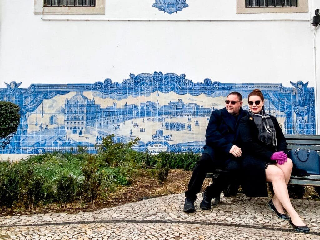 Couple in winter clothing sitting on a bench infront of a blue tiles fresco in Lisbon