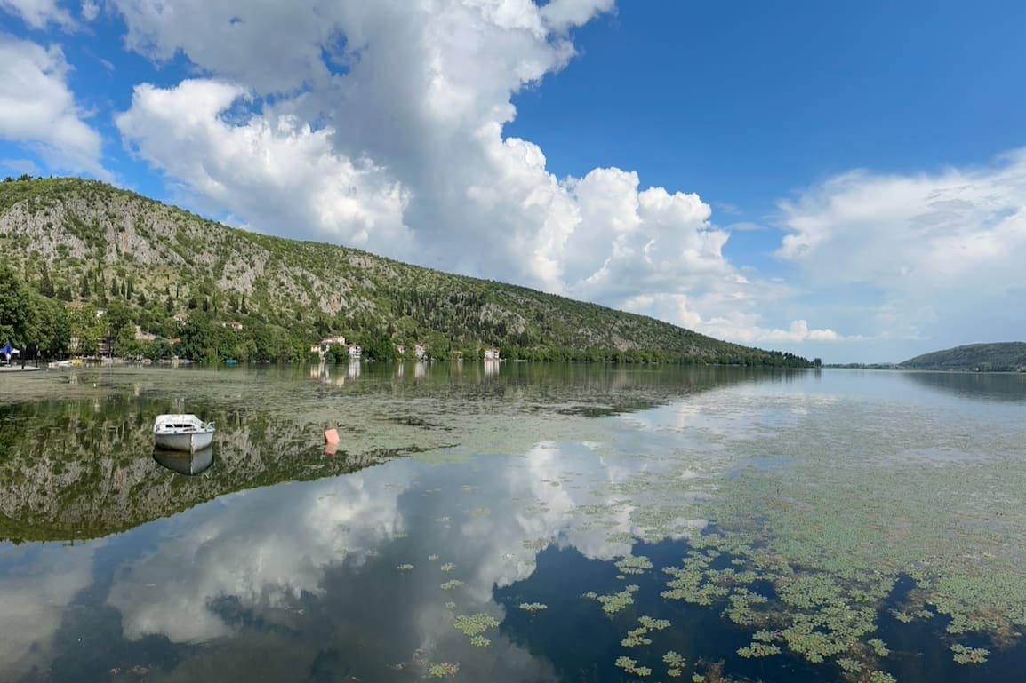 Lake of Orestiada with clouds in the sky and rolling hills in Kastoria. Photo by Paul Kostadimas © SpotlightSojourns.com