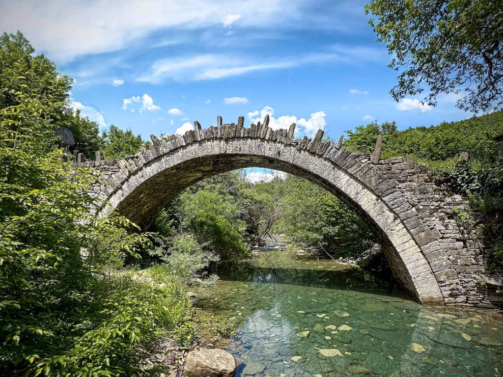 A stone bridge over a river with trees in the background.