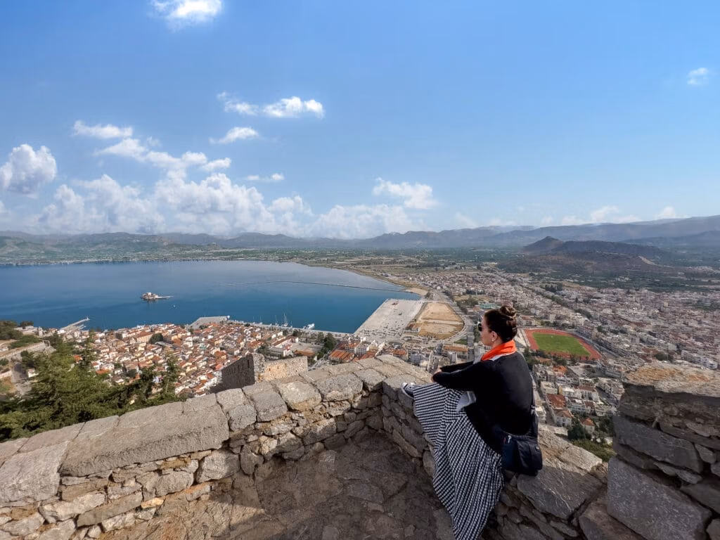 A man sitting on top of a stone wall overlooking the ocean.