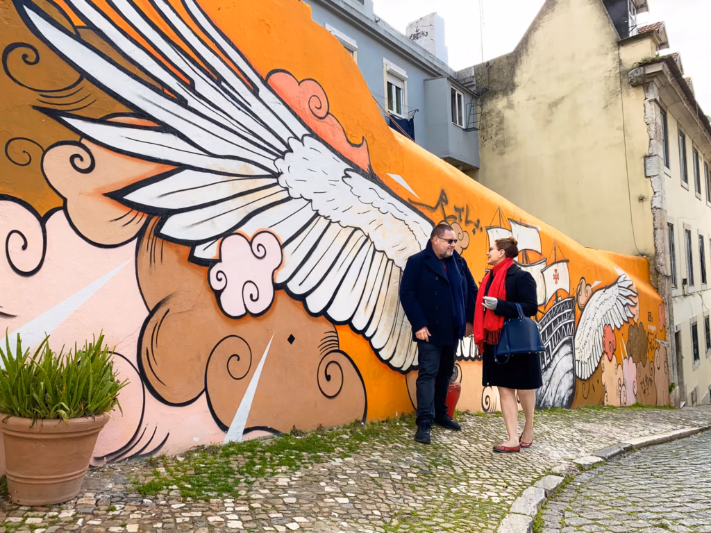 Two people standing in front of a mural on the side of a building.