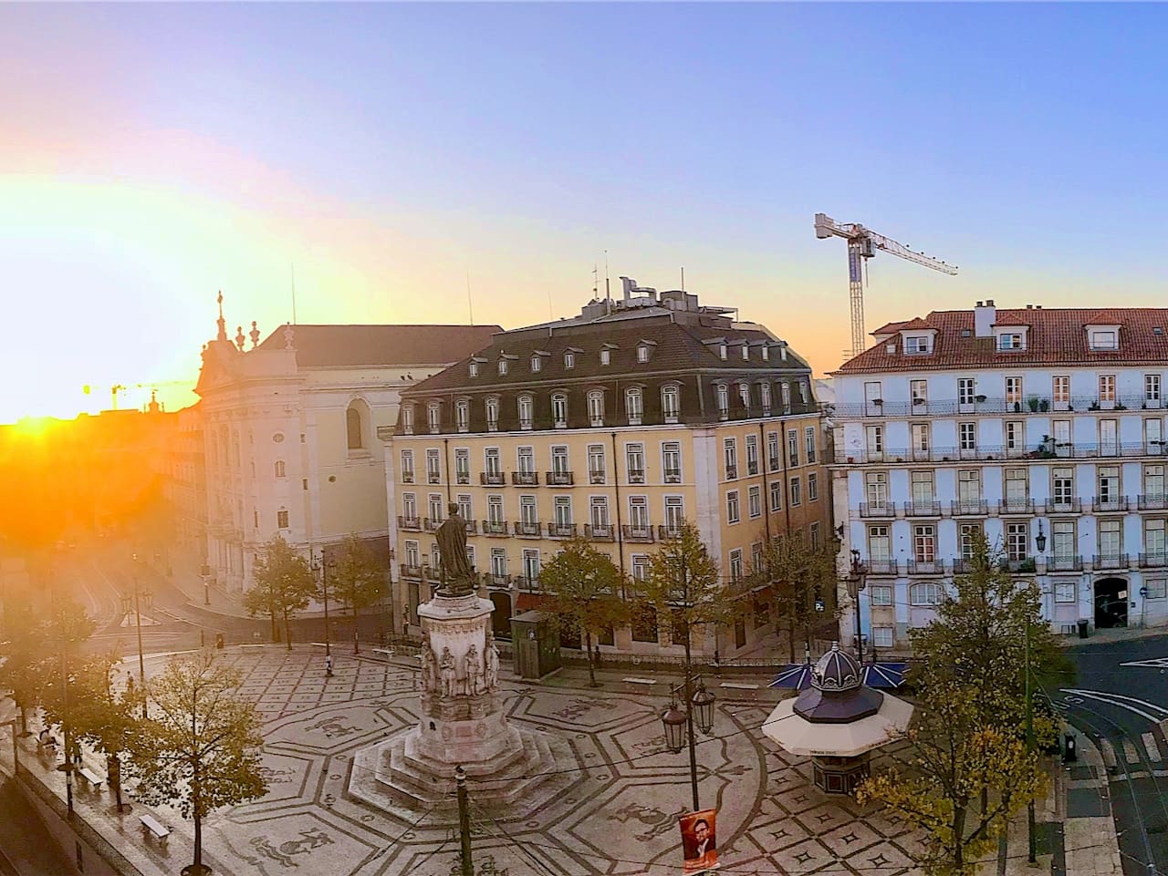 A view of the sun setting over a city over Luís de Camões Square