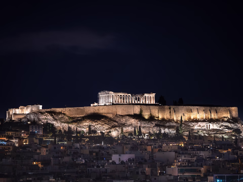 The ancient Acropolis of Athens and the Parthenon brilliantly illuminated at night against a dark evening sky.