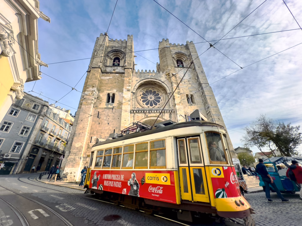 A yellow and red trolley car is driving past an old church.