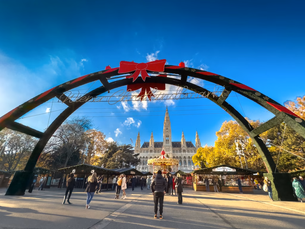 Exterior photo of a sunny winter's day infront of the decorated gates to the Rathausplatz Christkindlmarkt (Christmas market) at the Rathausplatz square.