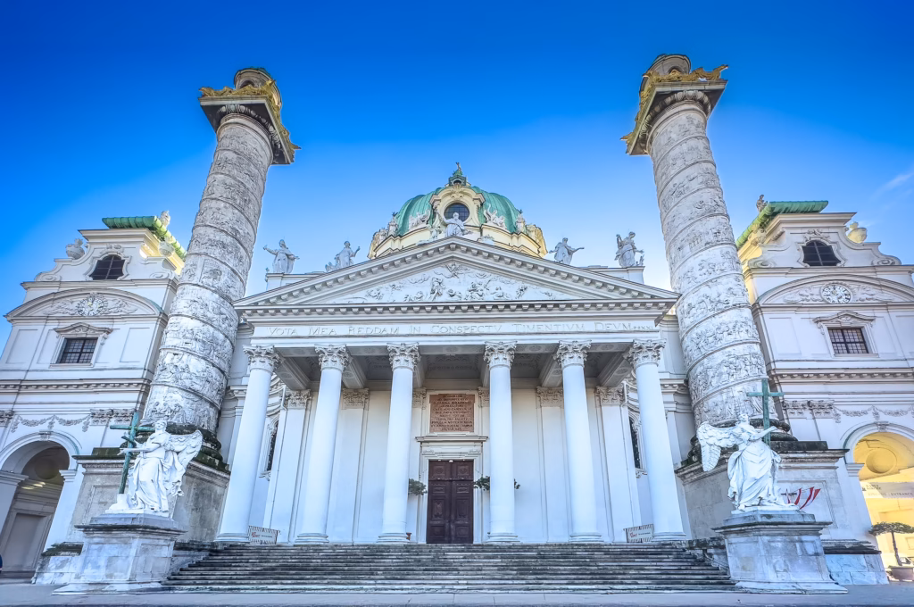 A large white building with columns and statues. The Christmas market in front of St Charles church at Karlsplatz is a locals favourite