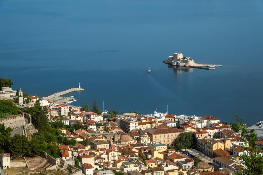 A view of the sea from above with buildings and boats, while Bourtzi castle is isolated by the surrounding sea in Nafpio Bay.