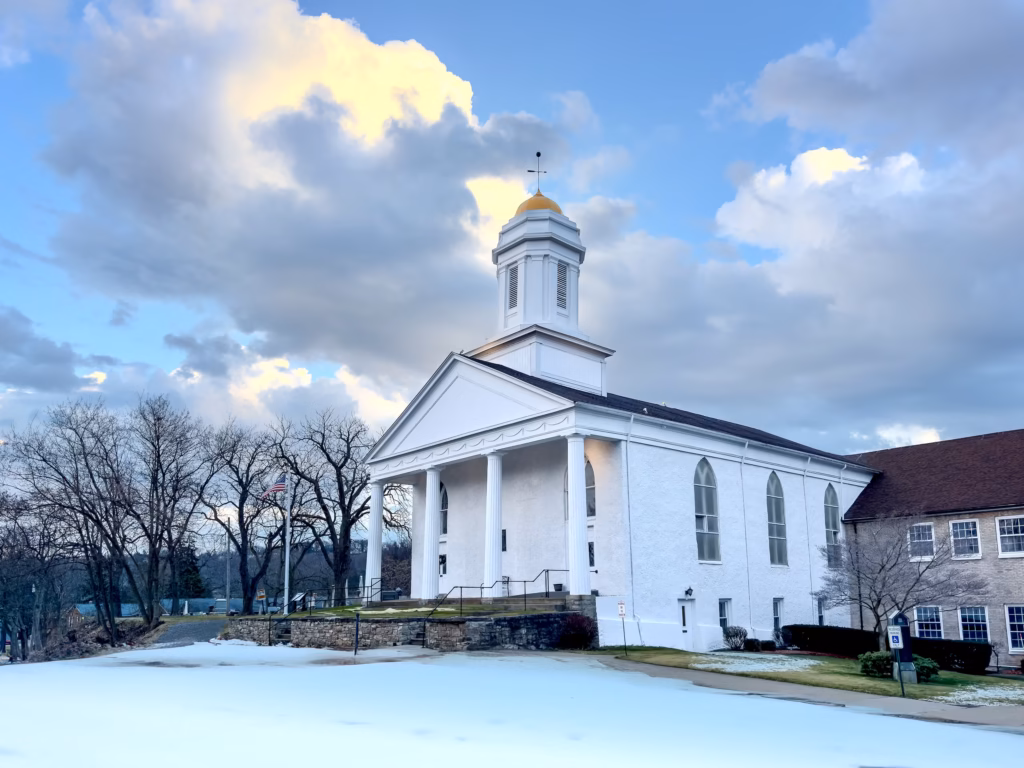 A church with snow on the ground and clouds in the sky.