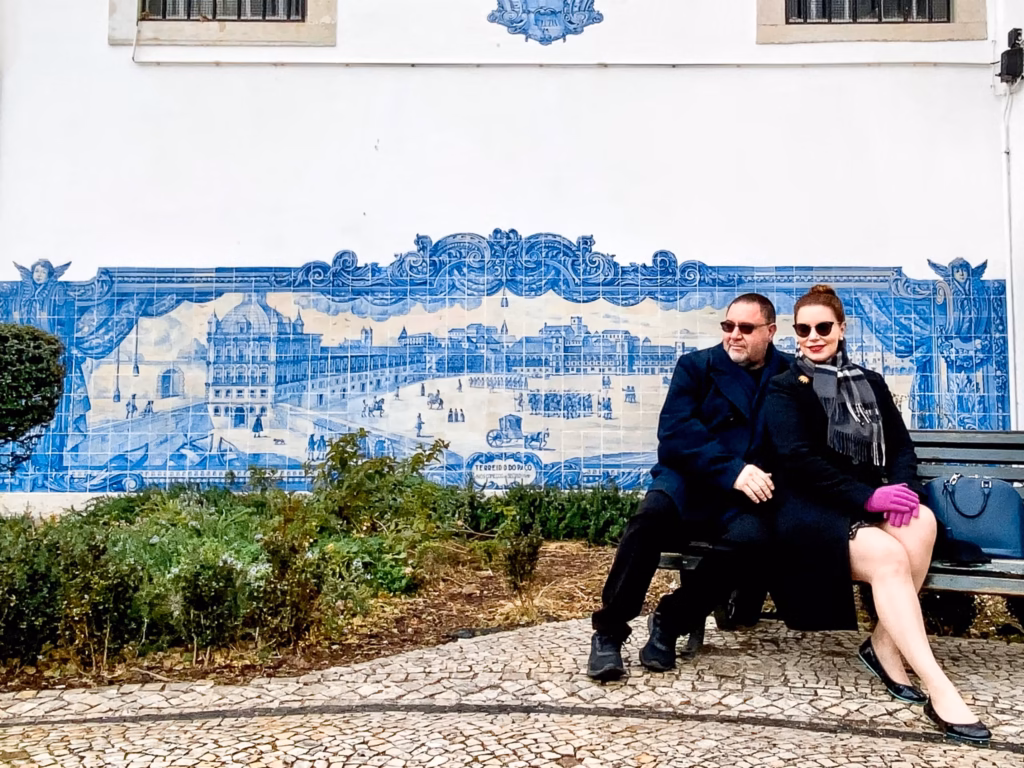 Couple in winter clothing sitting on a bench infront of a blue tiles fresco in Lisbon