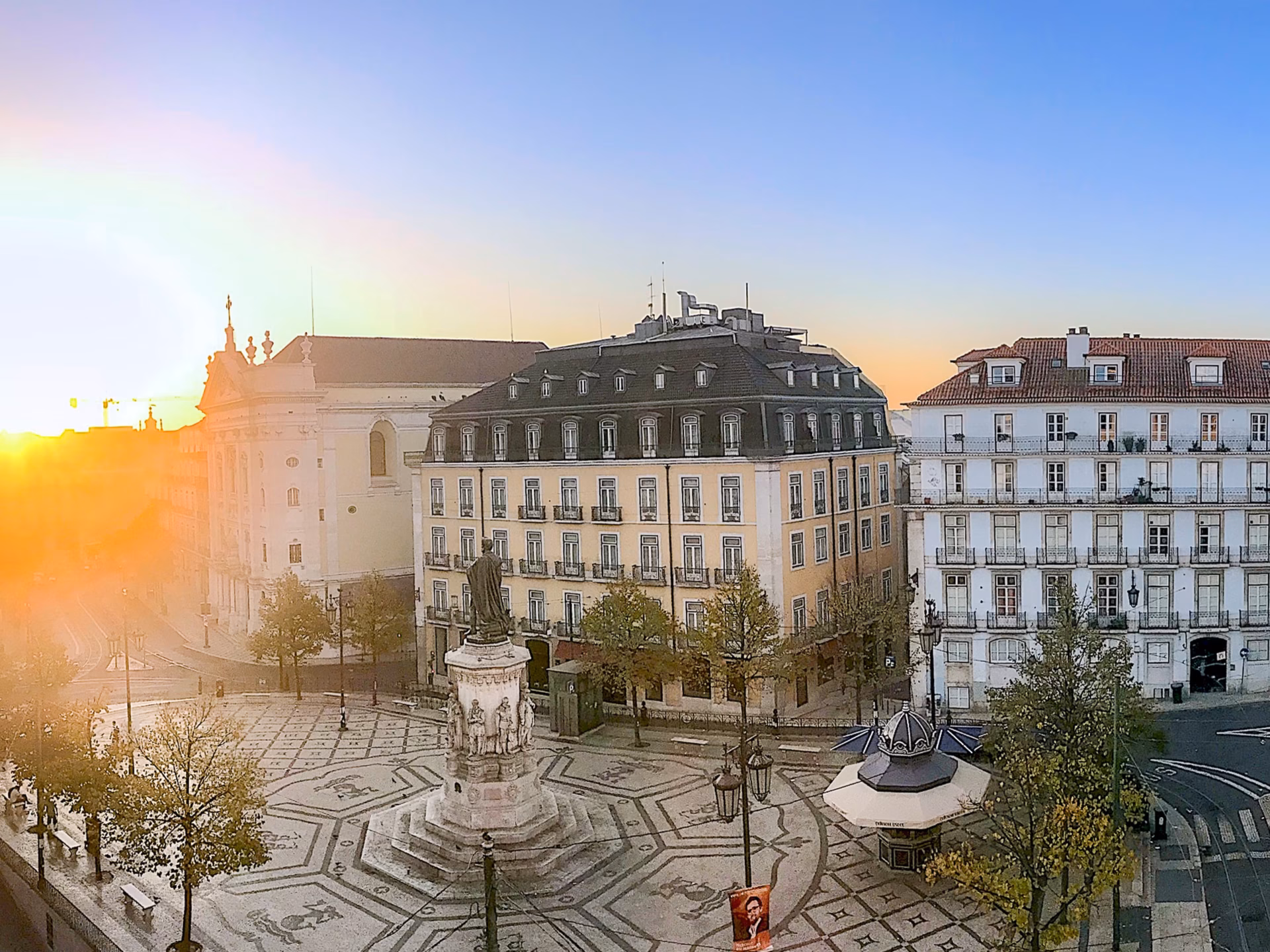 A view of the sun setting over a city over Luís de Camões Square
