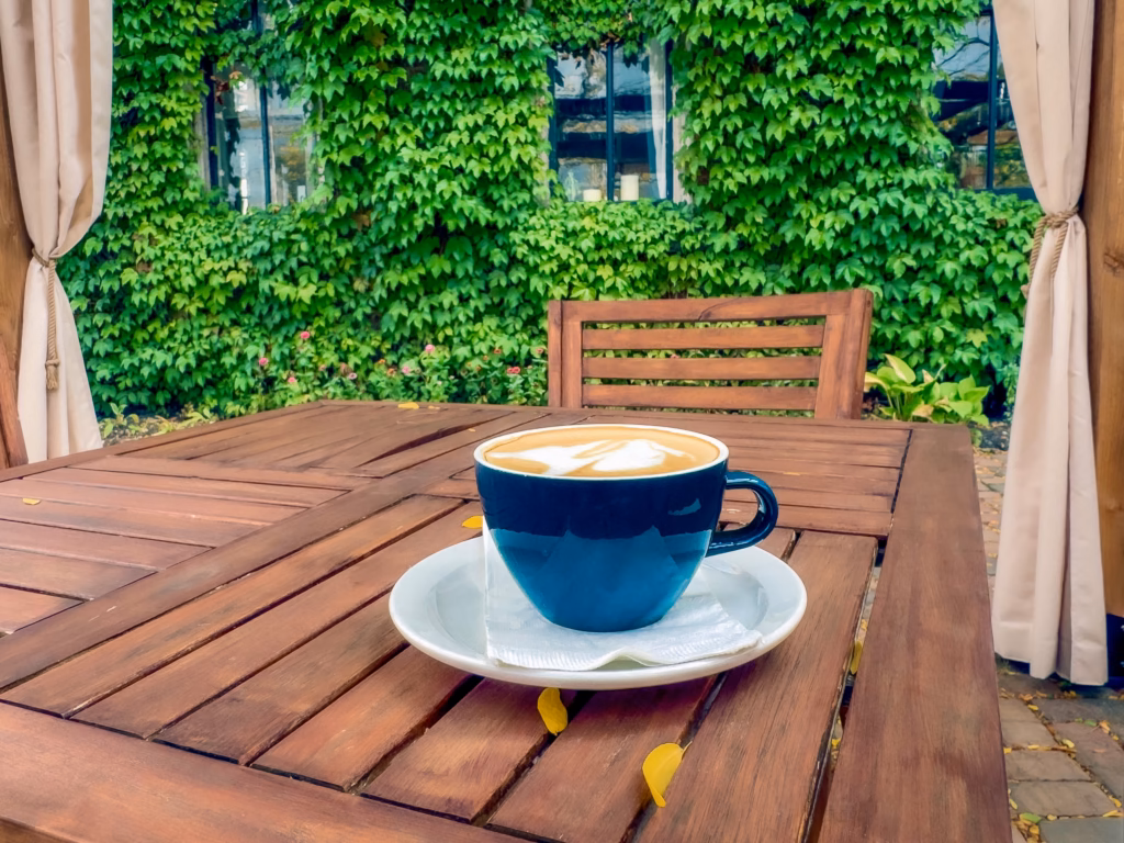A beautifully poured latte in a blue ceramic cup resting on a wooden patio table at Factory Espresso, an erie canal specialty coffee shop in Medina, New York.