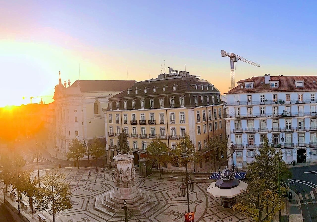 A view of the sun setting over a city over Luís de Camões Square